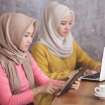 two woman wearing hijab are busy on their own gadget